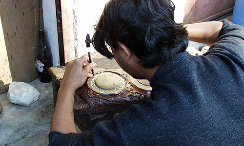 硬質樹脂をに埋め込んだ円形にくり抜いた銅板（「マニ車」の上ぶた）を彫金している職人さん